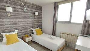 Habitación de hotel con dos camas, una pared de madera, una ventana, un televisor y una mesita de noche.