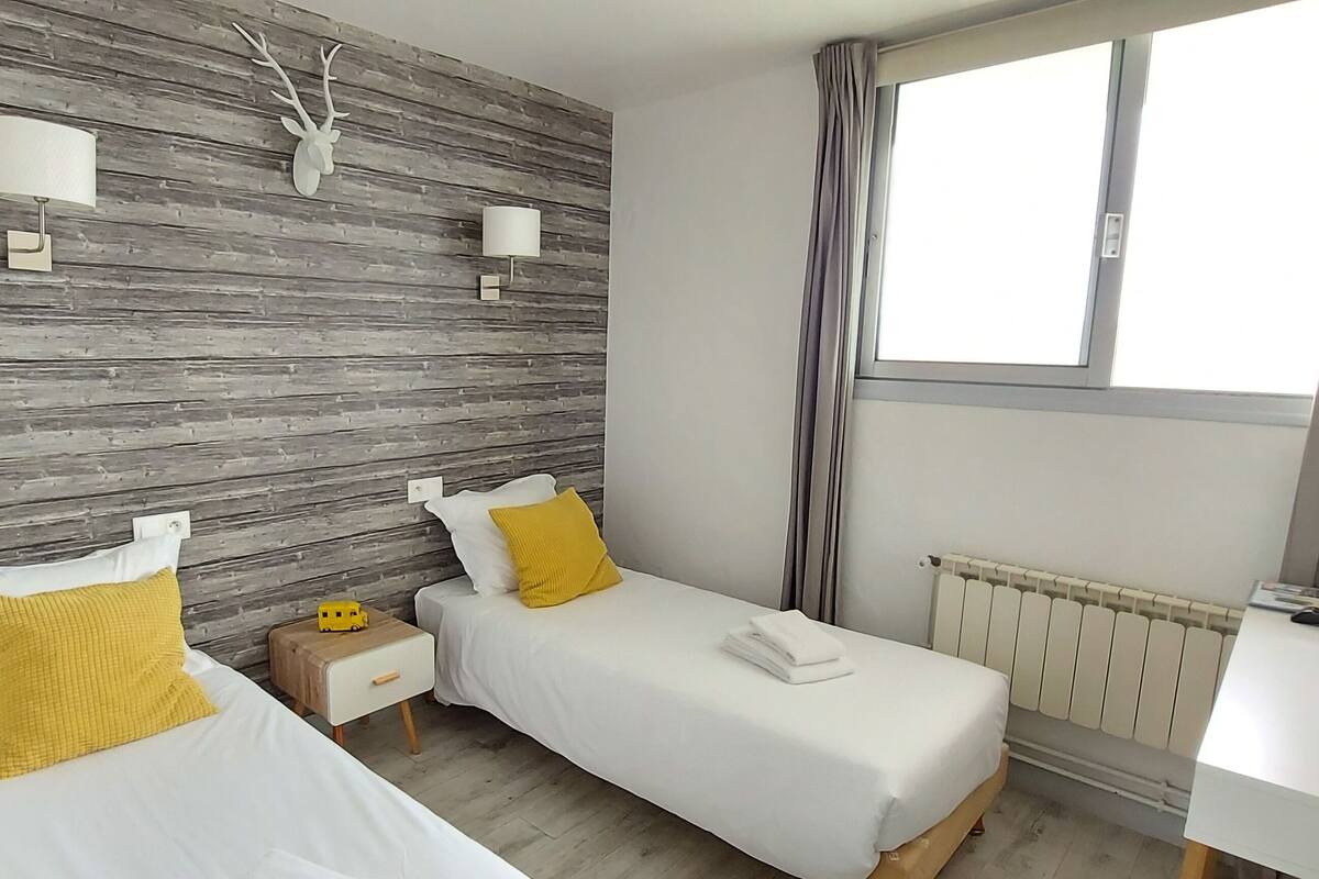 Habitación de hotel con dos camas, una pared de madera, una ventana, un televisor y una mesita de noche.