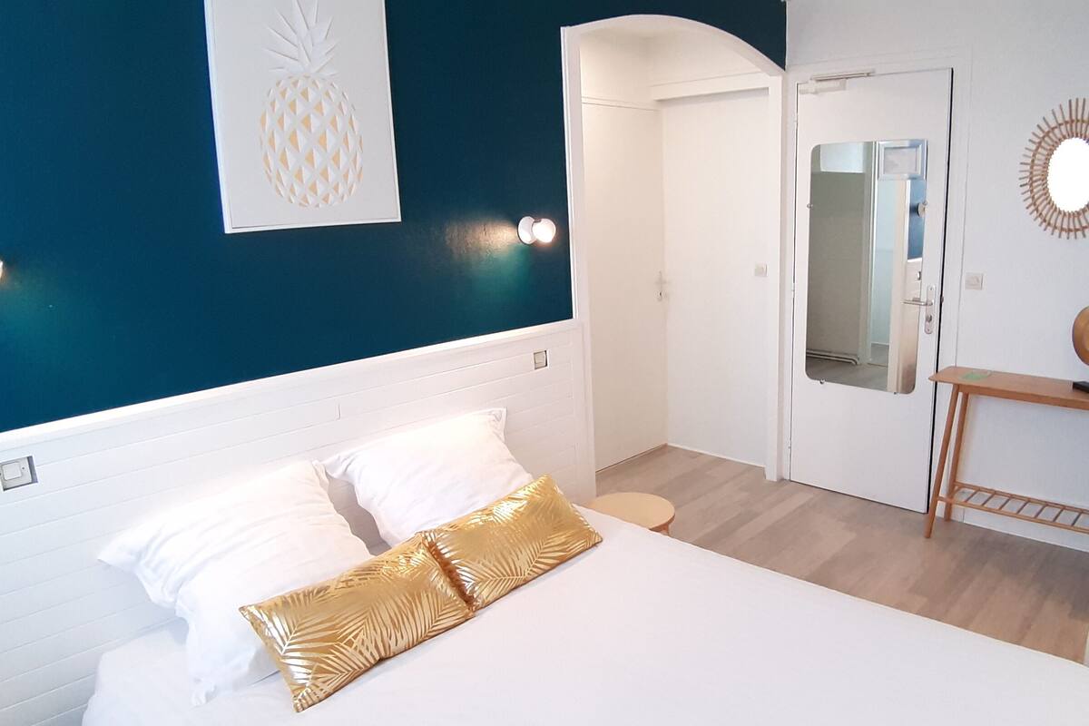 Un dormitorio con cama, mesita de noche, espejo y pared decorada con una piña.