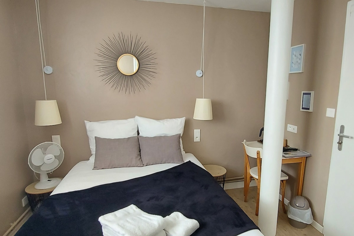 Ein Schlafzimmer mit einem Bett, Nachttischlampen, einem Wandspiegel, einem kleinen Tisch und einem Sessel.