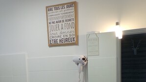 Un baño con un lavabo blanco, un perchero con dos toallas, un secador de pelo y un cartel con texto en francés en la pared.