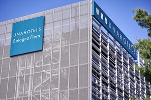 Um edifício com uma placa indicando 'UNAHOTELS Bologna Fiera' e um design arquitetônico moderno com fachada em estilo de grade.
