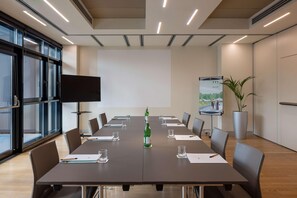 A conference room with a long table, chairs, a projector screen, a television, and a potted plant. - UNA Hotels Bologna Fiera (Bologna)