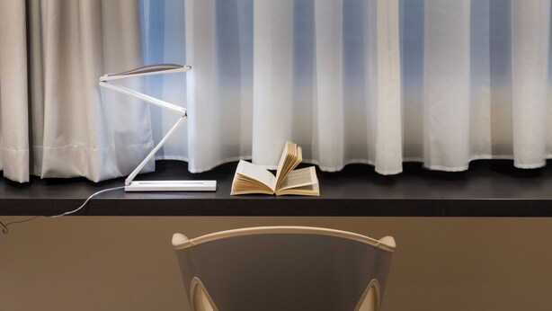 A desk with a lamp, an open book, and a chair in front of a window with curtains. - UNA Hotels Bologna Fiera (Bologna)