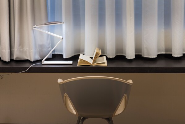Un bureau avec une lampe, un livre ouvert et une chaise devant une fenêtre ornée de rideaux.