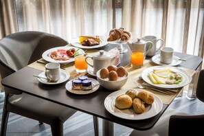 Mesa de café da manhã posta, com pratos de comida, um bule, xícaras e um copo de suco de laranja.
