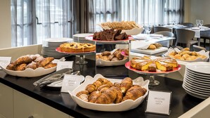 Un bufé con diversos productos horneados, incluyendo cruasanes y pasteles, dispuesto sobre una barra con platos y utensilios para servir.