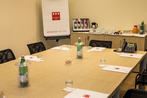 Une salle de conférence équipée d’une longue table, de chaises, d’un écran de projection et d’un coin café.