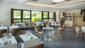 A restaurant with multiple tables and chairs, large windows with a view of greenery, and a wine rack with bottles. - UNA Hotels Bologna Fiera (Bologna)