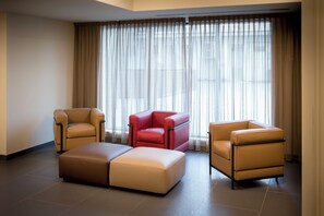 A modern hotel room with a sectional sofa, two armchairs, and a red accent chair. - UNA Hotels Bologna Fiera (Bologna)