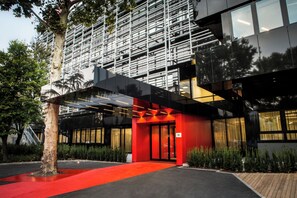 Un edificio moderno con entrada roja, un árbol en frente y una alfombra roja que lleva a la puerta.