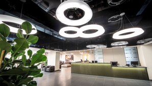 Un área de recepción moderna con mostrador verde, asientos y techo con lámparas circulares.