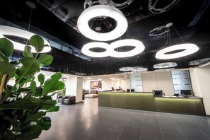 A modern reception area with a green counter, seating, and a ceiling with circular light fixtures. - UNA Hotels Bologna Fiera (Bologna)