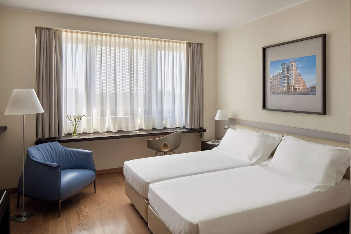 Hotellihuone, jossa on kaksi sänkyä, työpöytä, tuoli ja ikkuna, jossa on verhot.