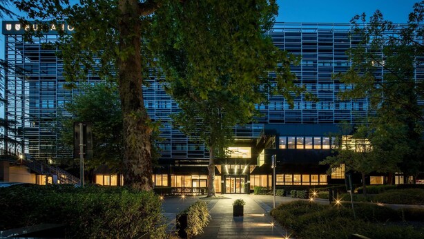 Un hotel moderno con fachada de vidrio, una entrada bien iluminada y un patio ajardinado.