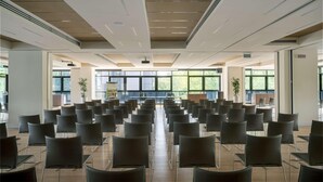 A conference room with rows of chairs, large windows, and ceiling vents. - UNA Hotels Bologna Fiera (Bologna)