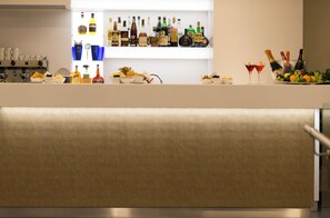 A bar area with various bottles and glasses, a fruit bowl, and a bottle of champagne. - UNA Hotels Bologna Fiera (Bologna)