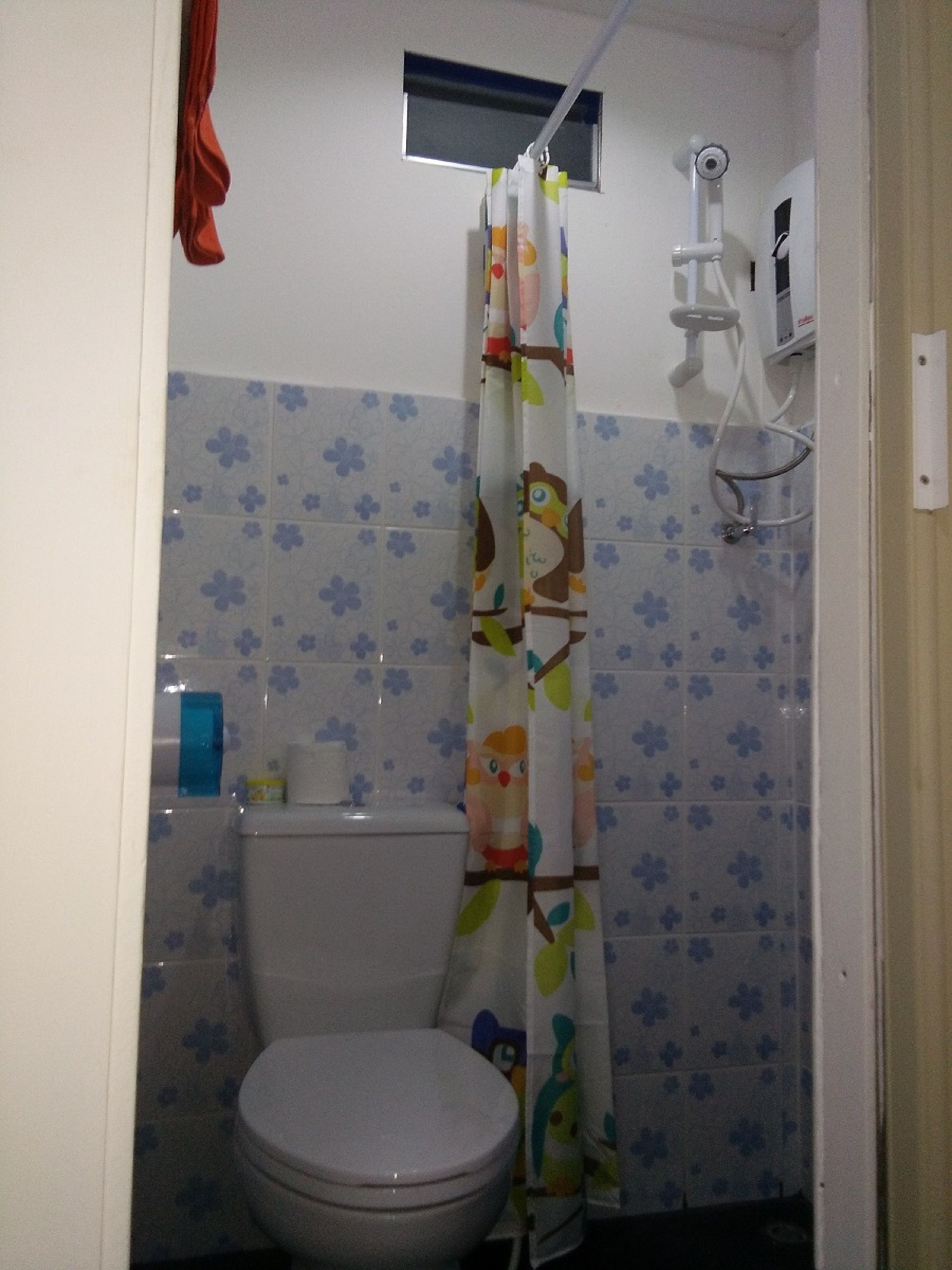 Ein kleines Badezimmer mit Toilette, einer Duschkabine mit Vogelmuster und einem Fenster über der Dusche.
