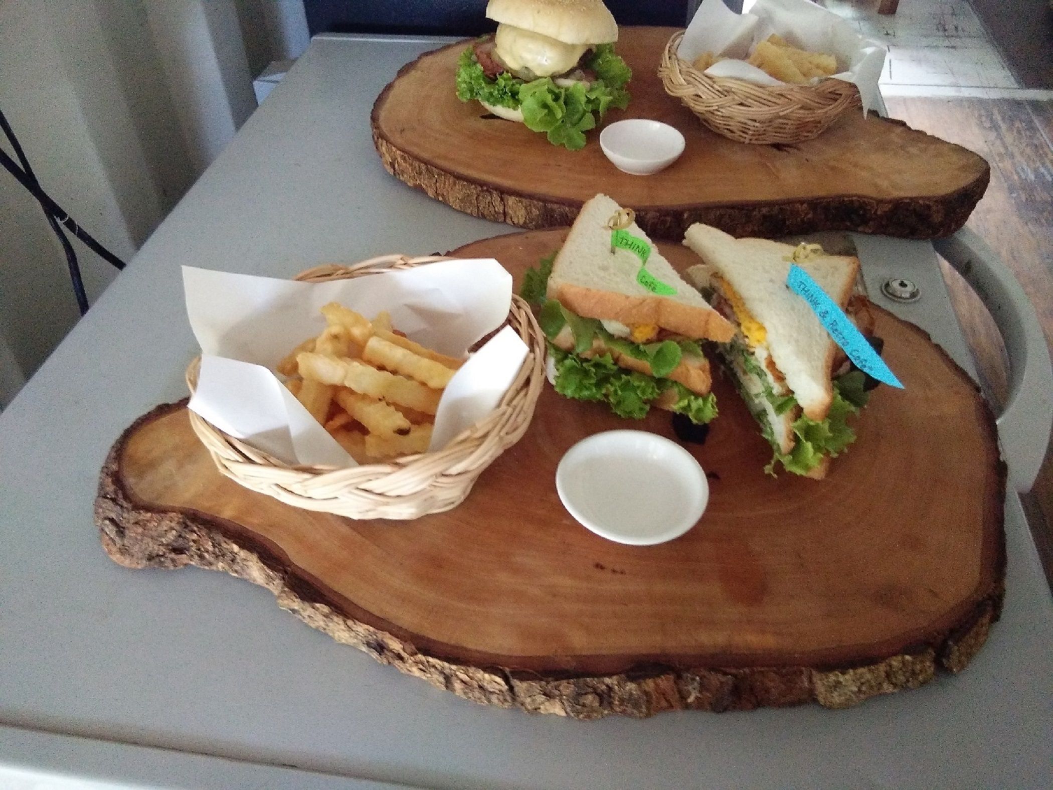 Een houten tafel met twee sandwiches en een mandje friet.