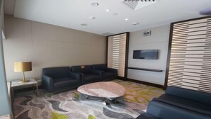 Une chambre d’hôtel moderne, dotée d’un canapé, d’une table basse ronde, d’un téléviseur fixé au mur et d’un tapis à motifs.