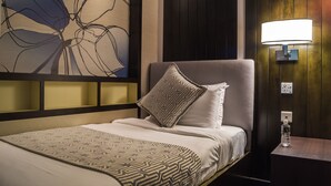 Une chambre d’hôtel avec un lit, une lampe fixée au mur et une bouteille d’eau sur une table de chevet.