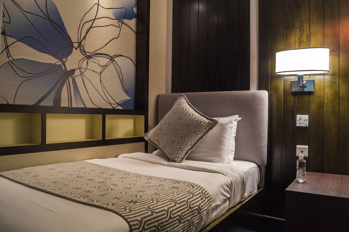 A hotel room with a bed, a wall-mounted lamp, and a water bottle on a nightstand.
