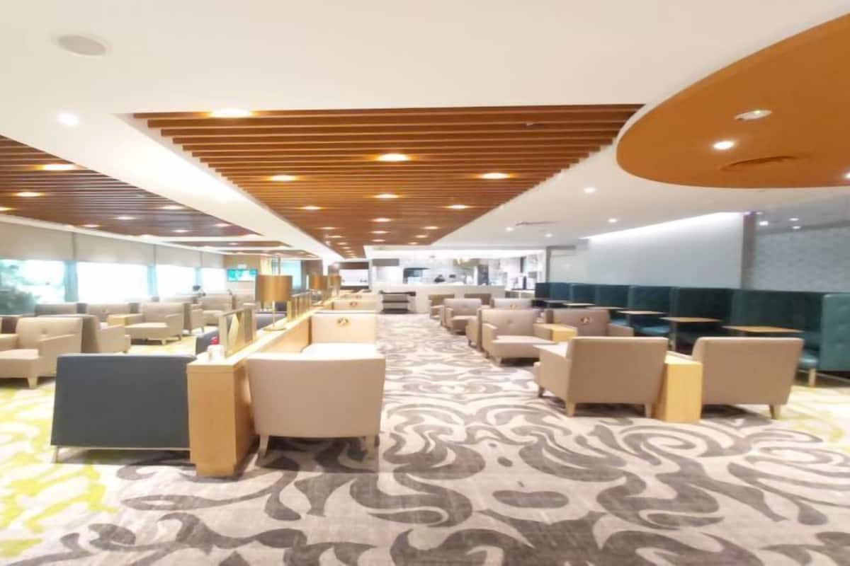 A spacious hotel lobby with multiple seating areas, a patterned carpet, and a modern ceiling design.
