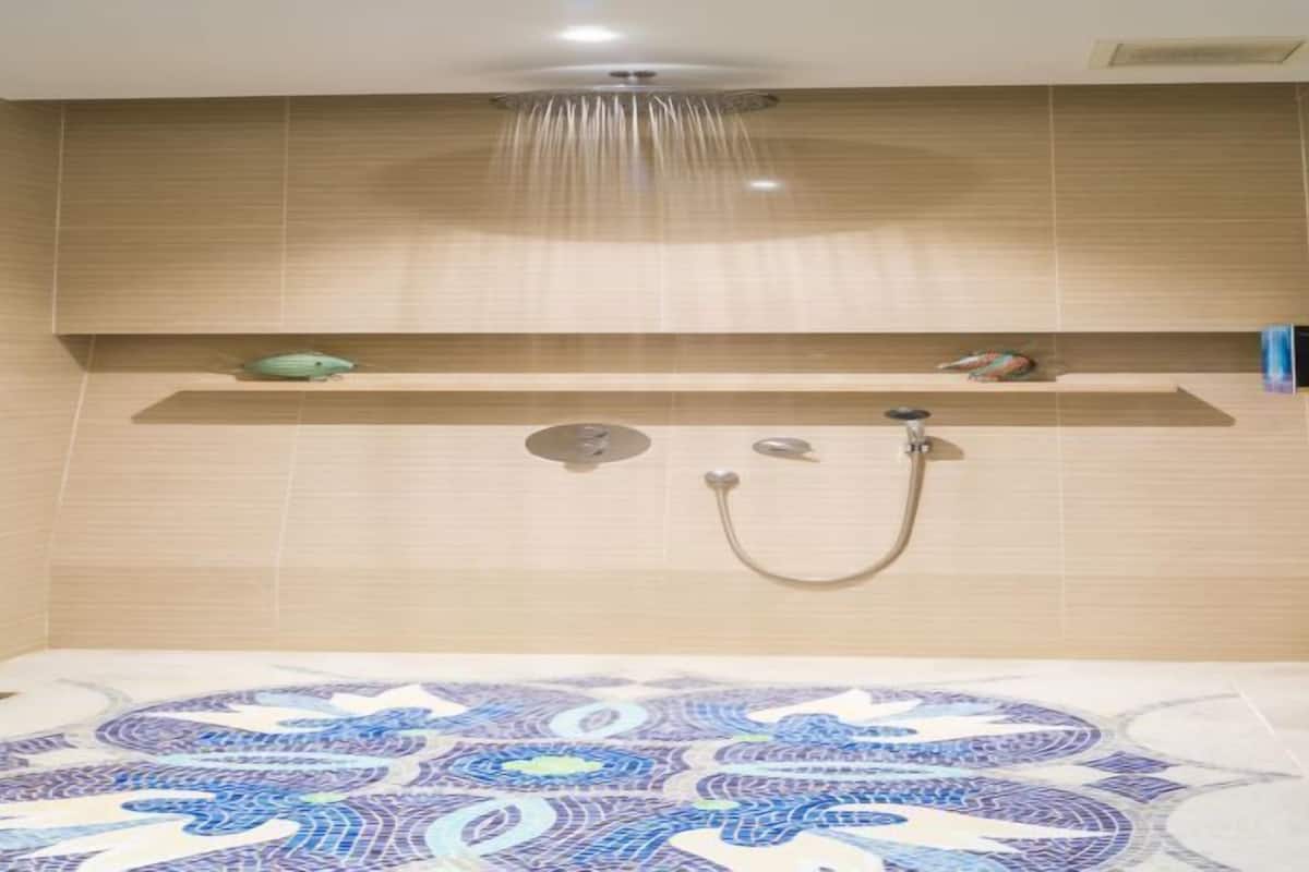 A modern shower area with a patterned floor, a wall-mounted shelf with decorative items, and a glass shower enclosure.