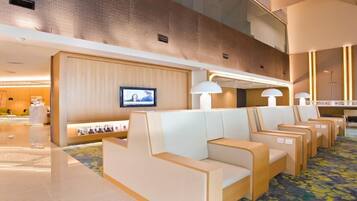 A hotel lobby with seating areas, a reception desk, and a television screen.