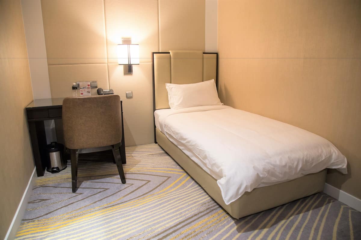 Una habitación de hotel con una cama, una silla, un escritorio y un cubo de basura.