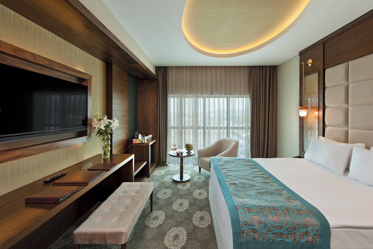 A hotel room with a large bed, a television, a desk with a vase of flowers, a chair, and a round table.