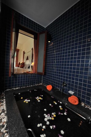 A bathroom with a black bathtub, blue tiled walls, a mirror, and a window with curtains. - Privacy Beach Resort and Spa (Sam Roi Yot)
