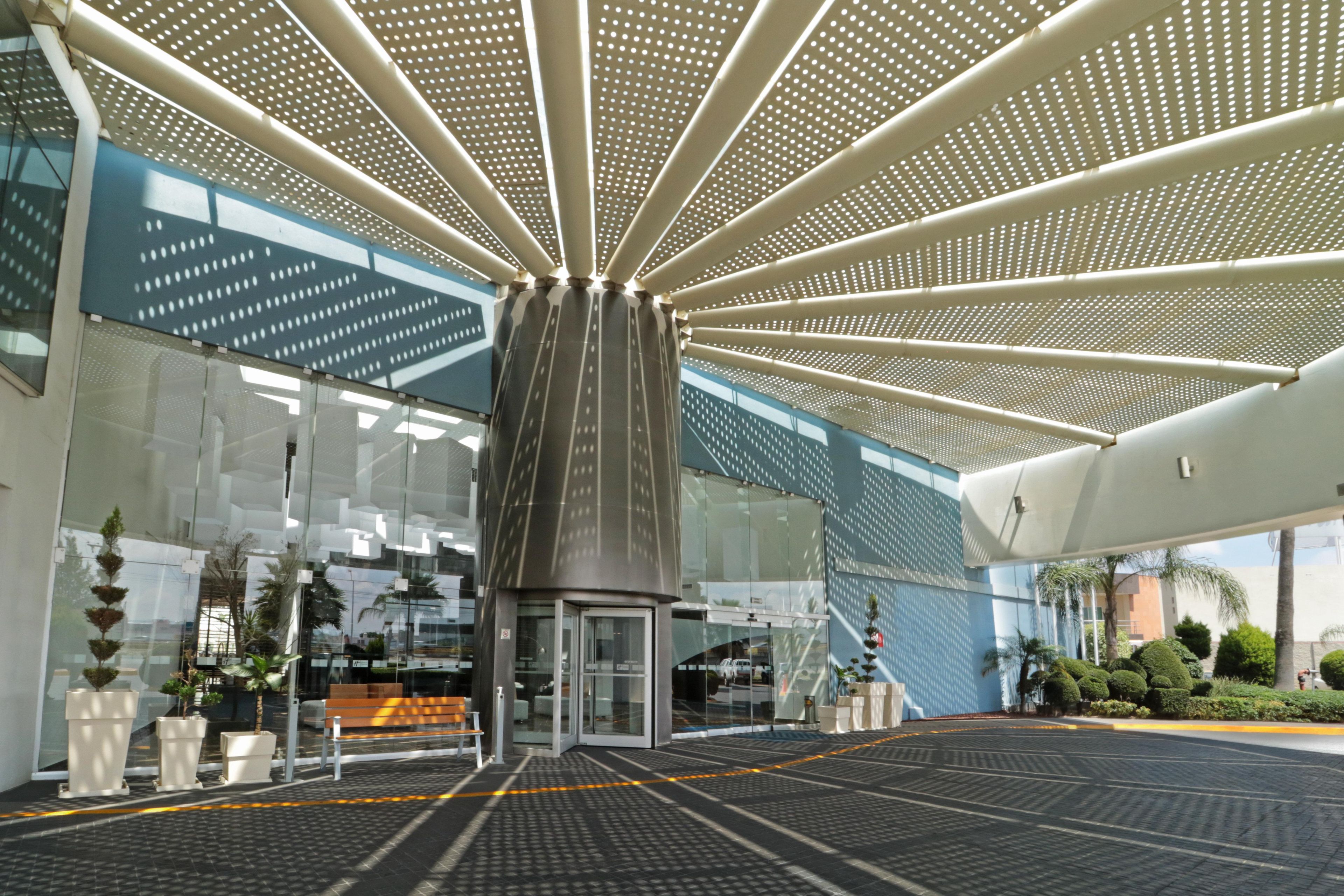 A modern building entrance with a glass facade, a central column, and a patterned ceiling.