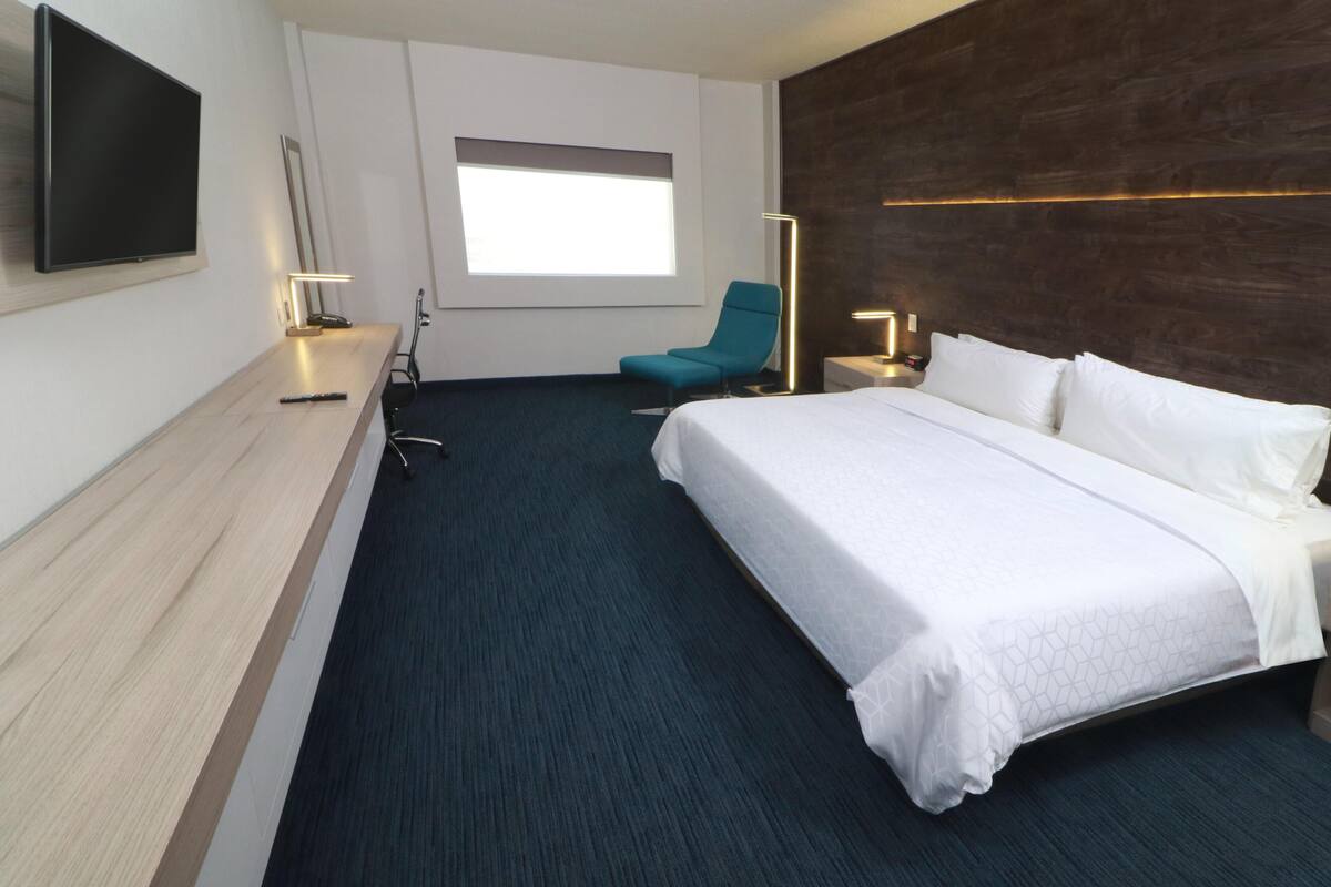 A hotel room with a large bed, a desk, a chair, a TV, and a window with a view.