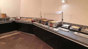 A buffet setup with various food stations, a marble-tiled floor, and a modern kitchen layout.