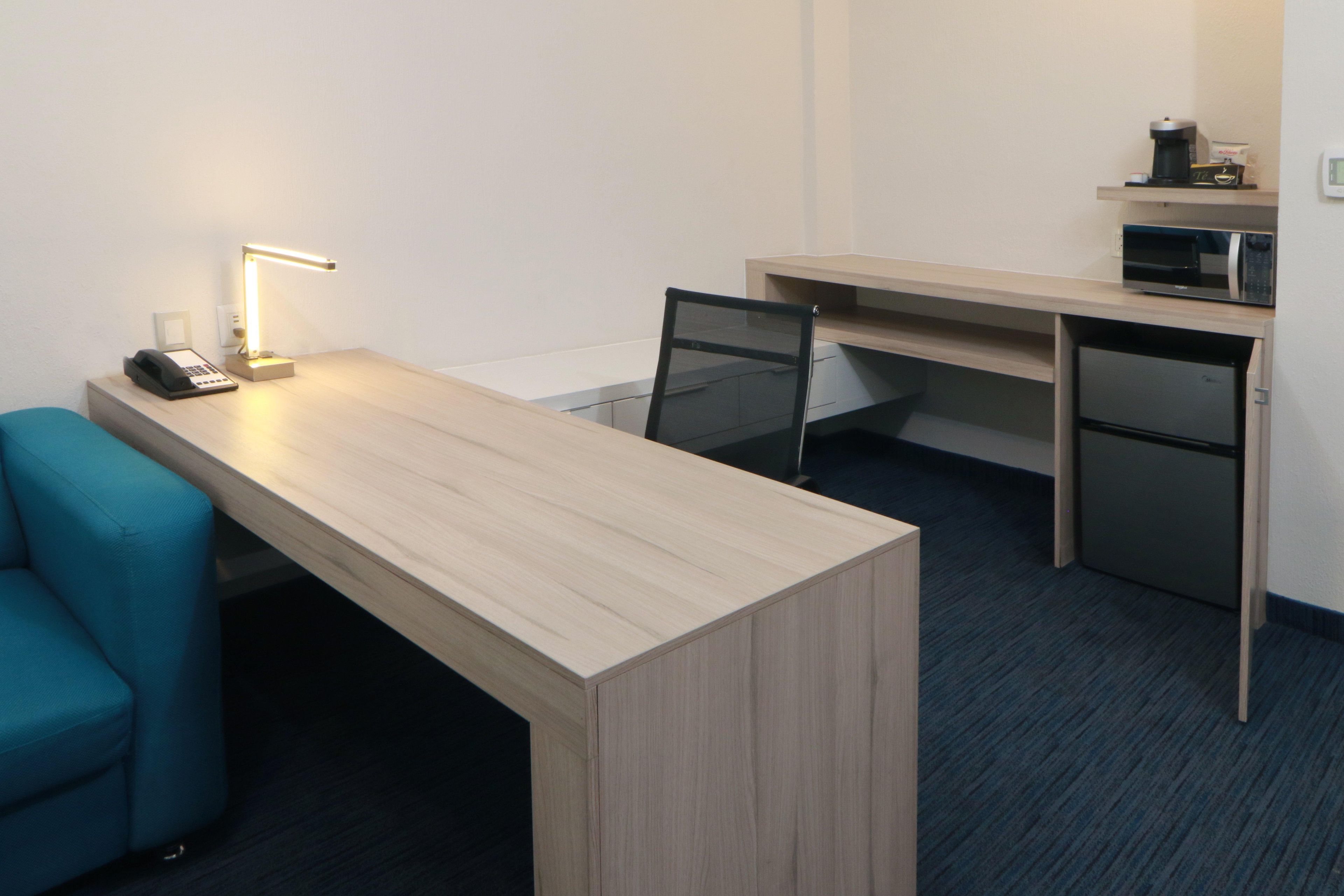 Een hotelkamer met een houten bureau, een stoel, een bureaulamp, een telefoon, een magnetron, en een klein plankje met een koffiezetapparaat.