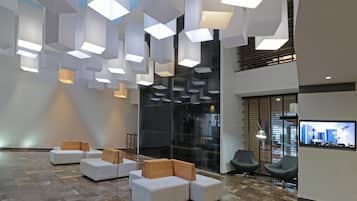 A modern lobby with geometric light fixtures, seating areas, and a television screen displaying a car showroom.