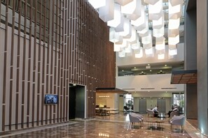 Um hall amplo com teto alto, luminárias modernas e um espaço de estar com mesas e cadeiras.