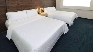A hotel room with two beds, a wooden headboard, a nightstand with a lamp, and a window.