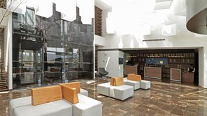 Eine moderne Lobby mit Sitzbereichen, einem Empfangstresen und einer Glasfassade.