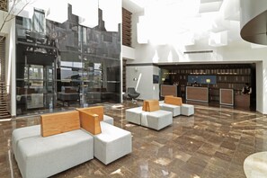 Eine moderne Lobby mit Sitzbereichen, einem Empfangstresen und einer Glasfassade.