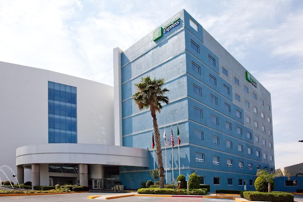 A modern hotel building with a prominent Express logo, multiple floors, and a well-maintained garden area.