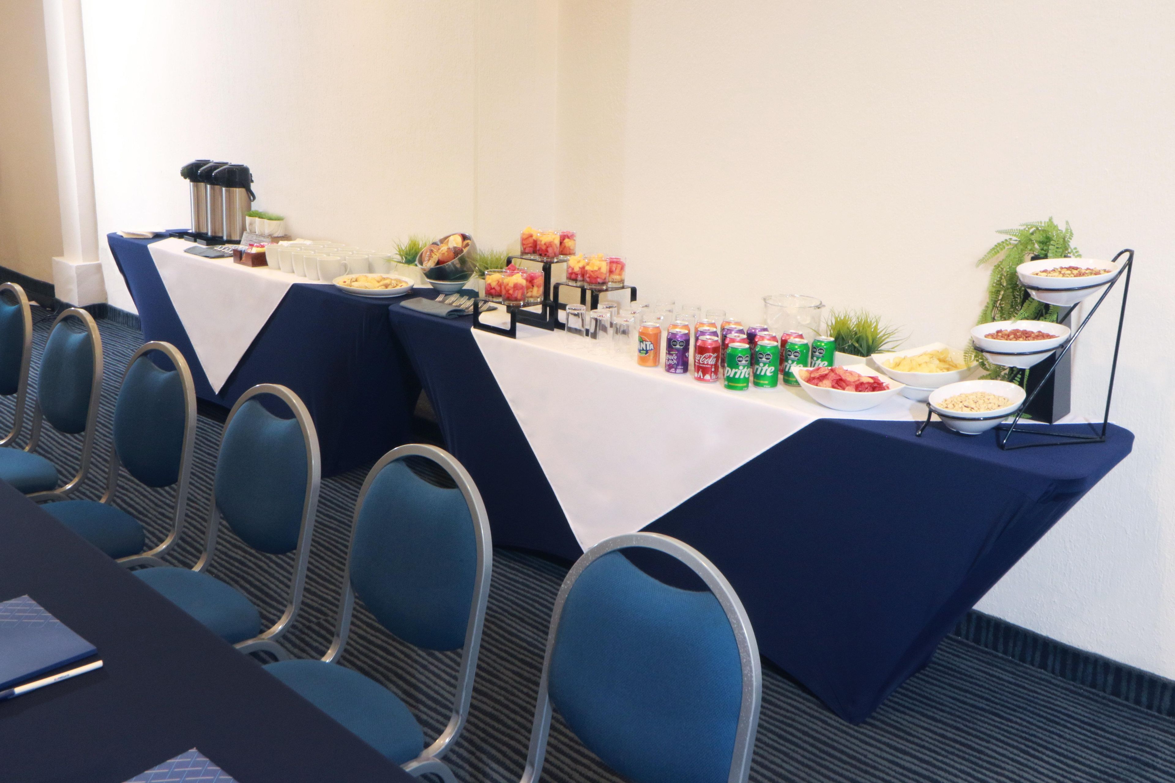 A conference room with a long table, blue chairs, and various food and drink options.