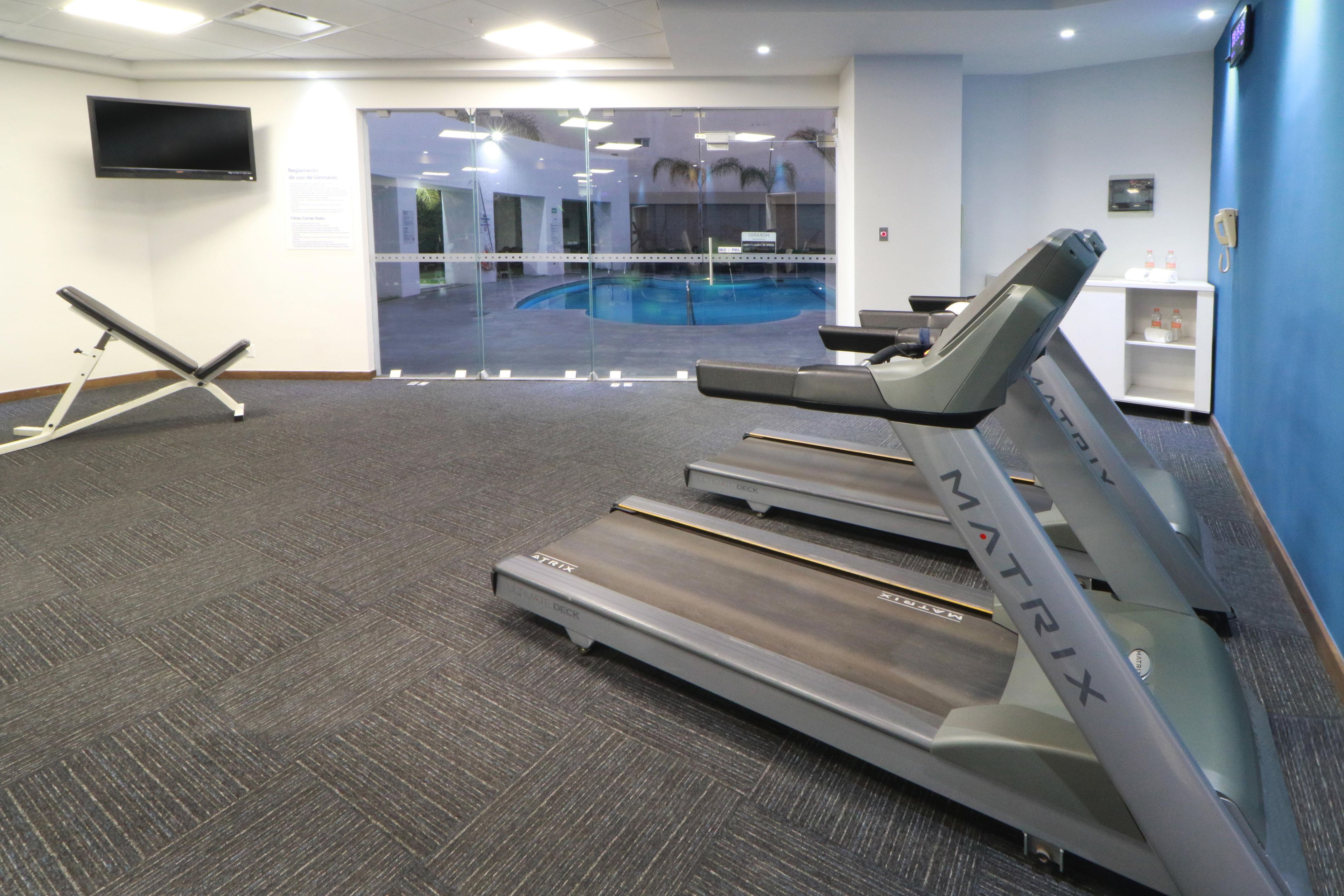 A gym with treadmills, a stationary bike, and a pool visible through a glass wall.