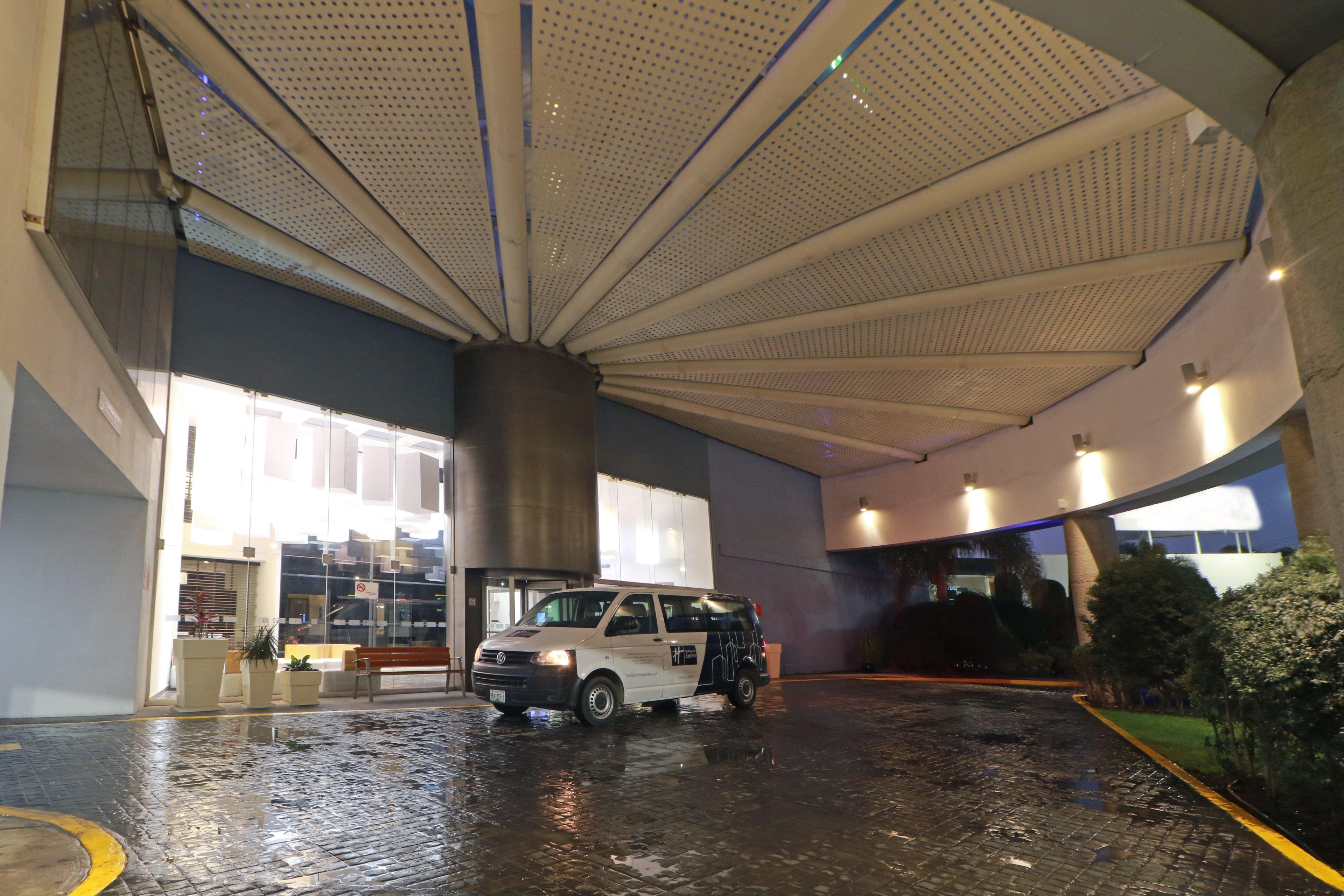 A white van parked inside a building with a large, perforated ceiling and a wet floor.