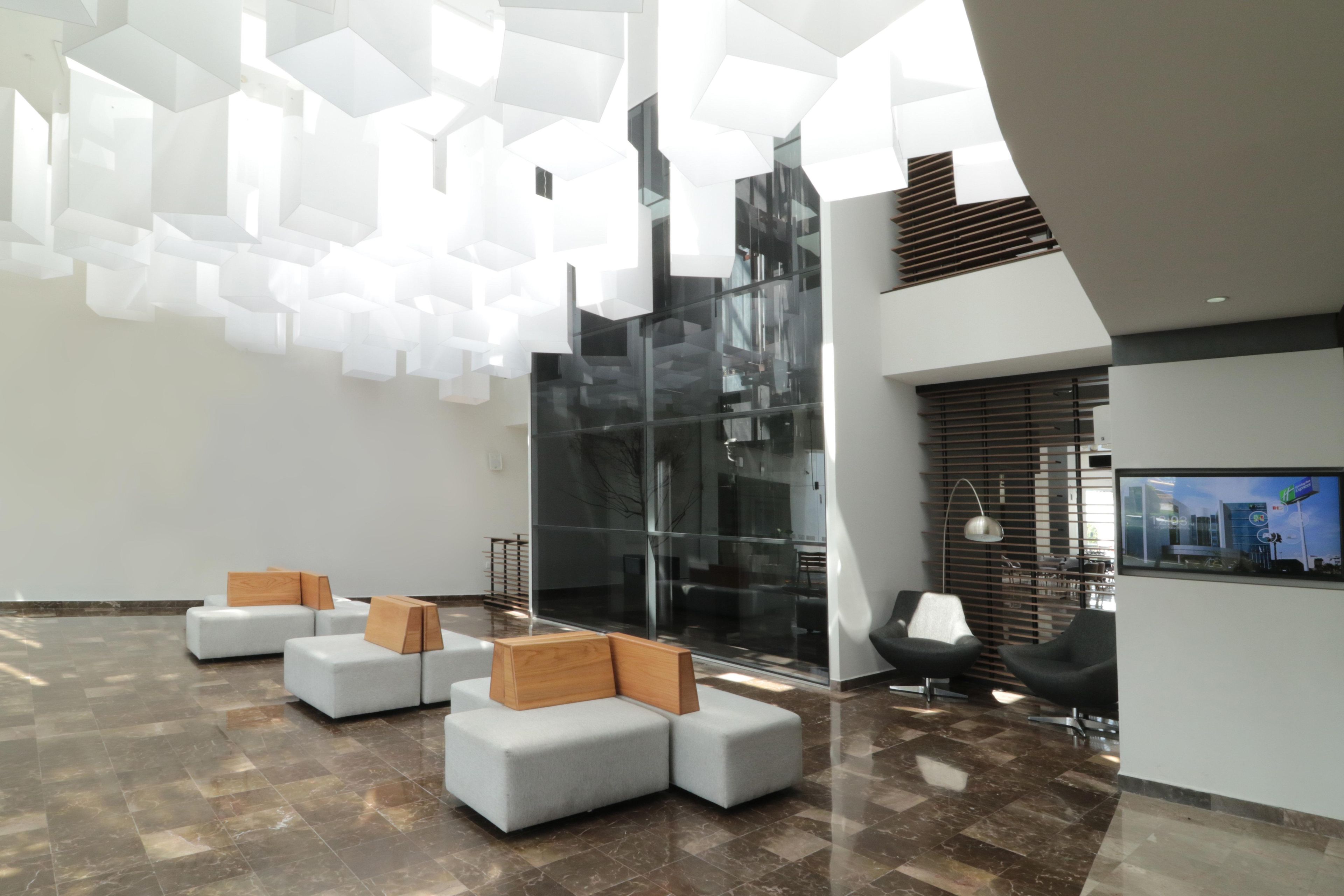 A modern lobby with geometric ceiling lights, a glass wall, and seating areas.