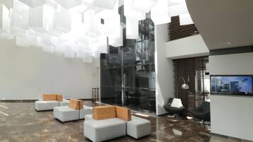 A modern lobby with geometric ceiling lights, a glass wall, and seating areas.