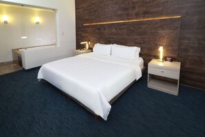 Quarto de hotel com cama grande, mesas de cabeceira, espelho e iluminação na parede.