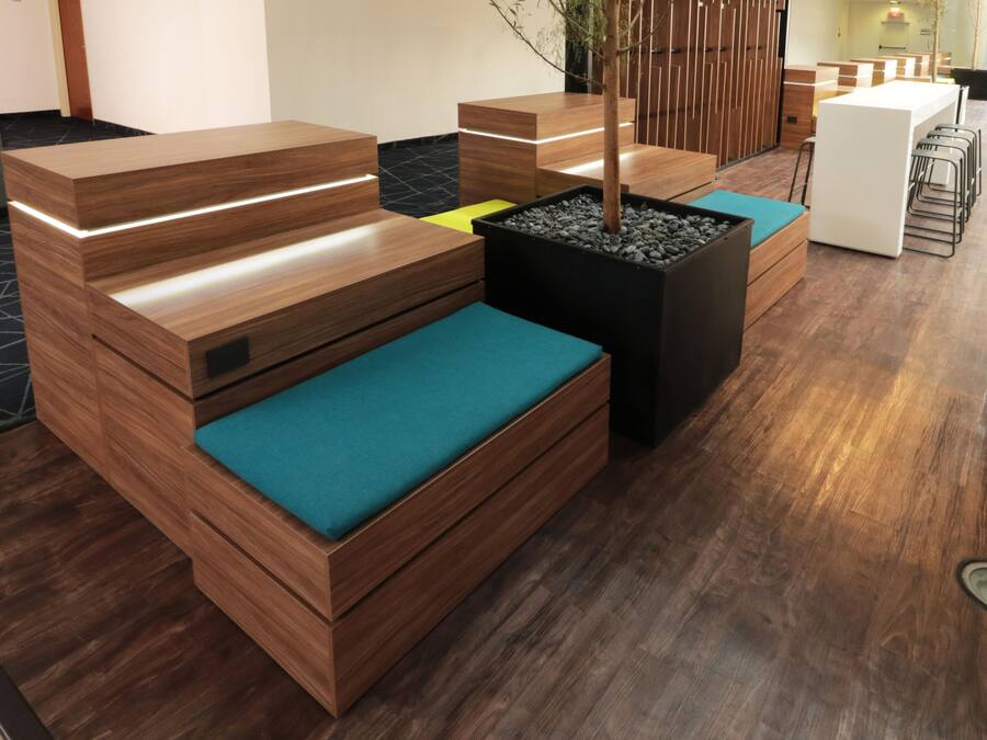 A modern reception area with wooden furniture, a potted plant, and a seating area with teal cushions.
