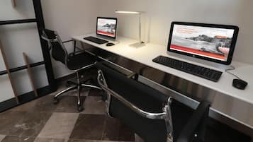 A modern office space with two desks, each with a computer, keyboard, and mouse. There are two office chairs, a standing desk, and a floor lamp.